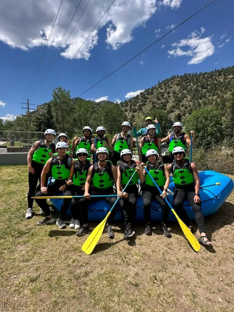 A group of rafters on a shored raft posing for a photo.