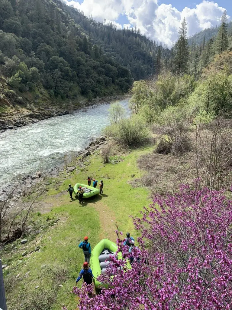 Two groups of people walking green rafts to the river with mountains in the background.